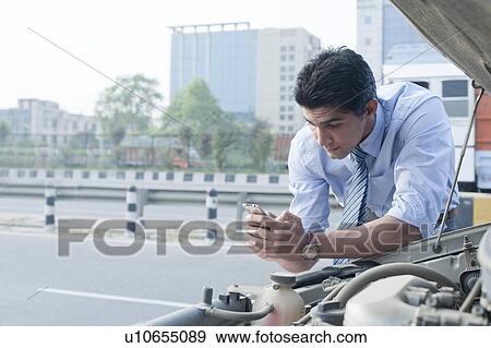 Stock Photo - Businessman using a mobile phone near a broken down car, Gurgaon, Haryana, India. Fotosearch