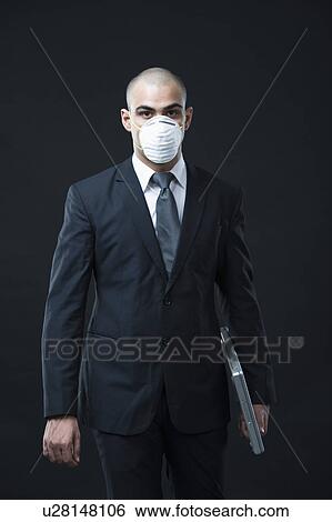 Businessman wearing a pollution mask and holding a laptop View Large Photo Image Stock Photograph - Businessman wearing a pollution mask and holding a laptop. Fotosearch