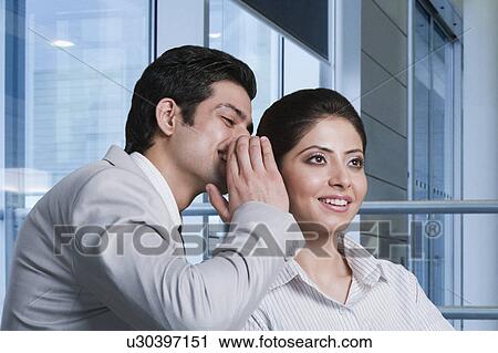 Stock Image - Businessman whispering to a businesswoman. Fotosearch