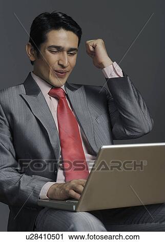 Stock Image - Businessman working on a laptop and clenching fist. Fotosearch