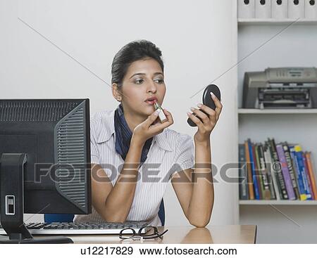 Stock Photo - Businesswoman applying lipstick in an office. Fotosearch