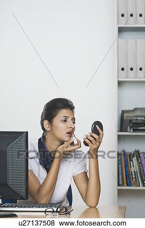 Stock Photo - Businesswoman applying lipstick in an office. Fotosearch