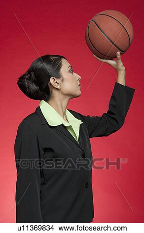 Picture - Businesswoman holding a basketball as though aiming for a shoot. Fotosearch