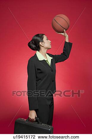 Stock Image - Businesswoman holding a basketball as though aiming for a shoot. Fotosearch