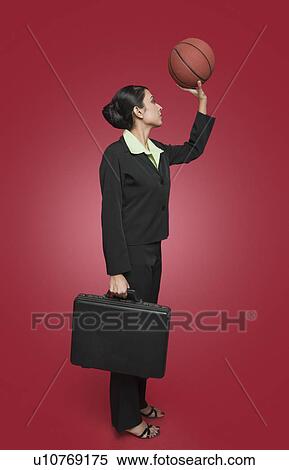 Stock Photography - Businesswoman holding a basketball as though aiming for a shoot. Fotosearch