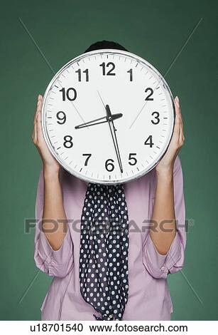 Stock Image - Businesswoman holding a clock in front of her face. Fotosearch