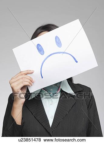Businesswoman holding a sad face in front of her face View Large Photo Image Stock Photo - Businesswoman holding a sad face in front of her face. Fotosearch