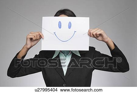 Picture - Businesswoman holding a smiley face in front of her face. Fotosearch
