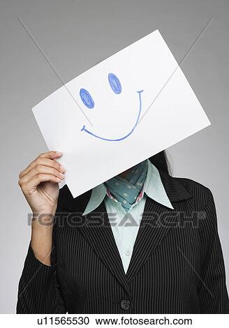 Businesswoman holding a smiley face in front of her face View Large Photo Image Stock Image - Businesswoman holding a smiley face in front of her face. Fotosearch