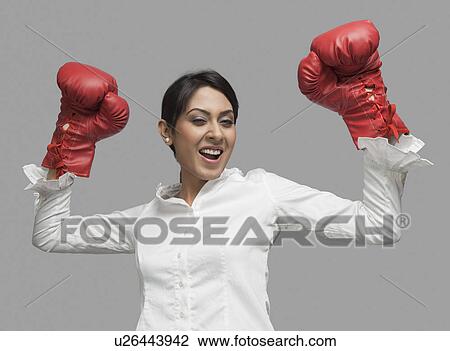 Stock Image - Businesswoman in boxing gloves cheering with arms raised. Fotosearch