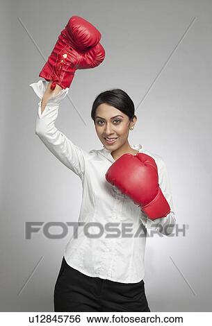 Businesswoman in boxing gloves cheering with hand raised View Large Photo Image Stock Photograph - Businesswoman in boxing gloves cheering with hand raised. Fotosearch