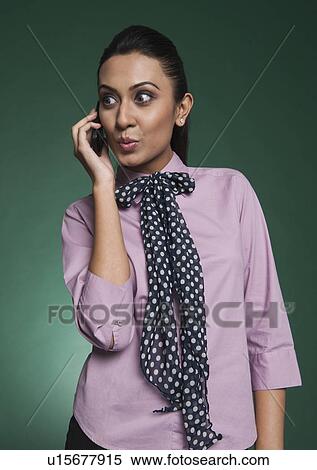 Stock Photography - Businesswoman looking surprised while talking on a mobile phone. Fotosearch