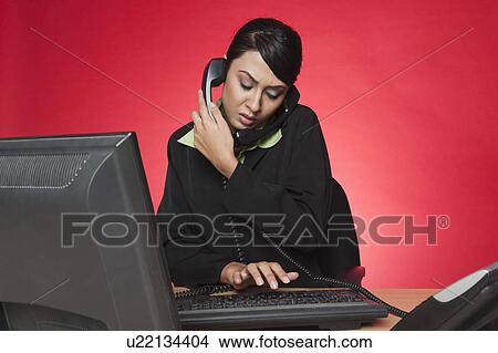 Businesswoman using a desktop pc while talking on multiple landline phones View Large Photo Image Picture - Businesswoman using a desktop pc while talking on multiple landline phones. Fotosearch