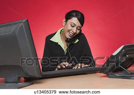 Businesswoman using a desktop pc while talking on a landline phone View Large Photo Image Stock Photo - Businesswoman using a desktop pc while talking on a landline phone. Fotosearch