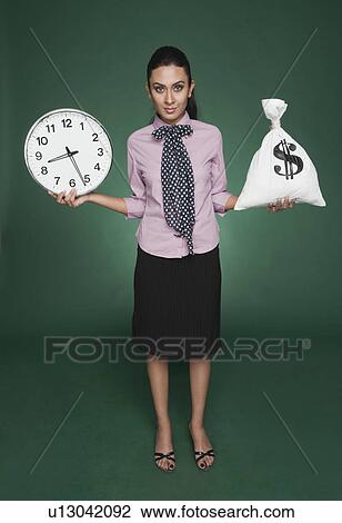 Stock Image - Businesswoman weighing time versus money. Fotosearch
