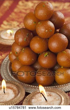 Stock Image - Candles burning around a tray of gulab jamuns. Fotosearch