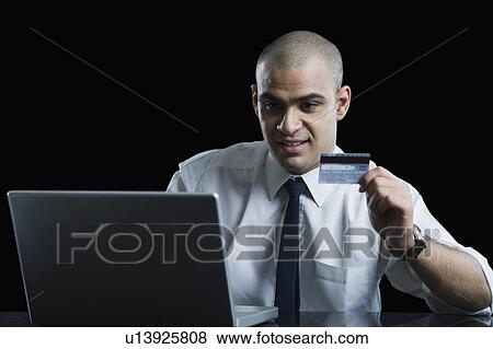 Stock Photo - Close-up of a businessman holding a credit card and using a laptop. Fotosearch