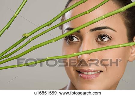 Stock Photo - Close-up of a woman with rose stems in front of her face. Fotosearch
