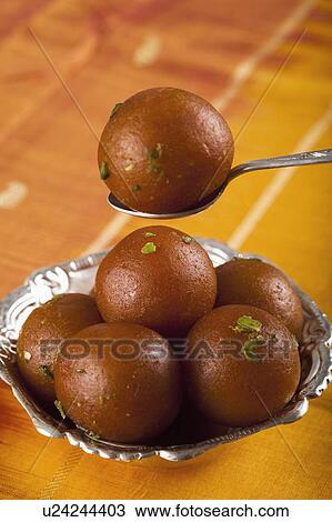 Stock Image - Close-up of gulab jamun in spoon over a bowl of gulab jamuns. Fotosearch