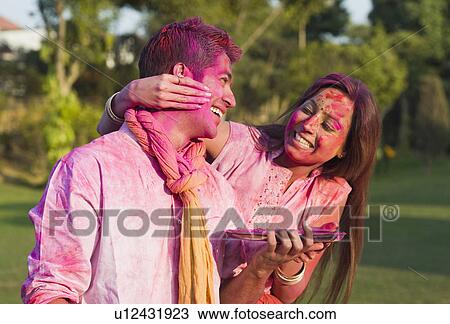 Stock Image - Couple celebrating Holi in a garden. Fotosearch
