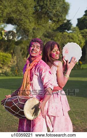 Stock Image - Couple celebrating Holi with musical instruments in a garden. Fotosearch