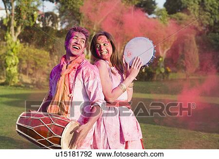 Stock Image - Couple celebrating Holi with musical instruments in a garden. Fotosearch