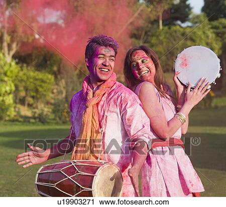 Stock Image - Couple celebrating Holi with musical instruments in a garden. Fotosearch