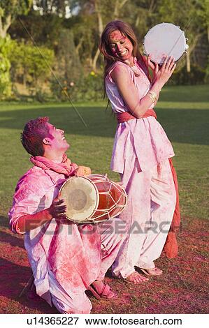 Stock Photo - Couple celebrating Holi with musical instruments in a garden. Fotosearch