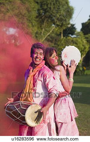 Stock Photograph - Couple celebrating Holi with musical instruments in a garden. Fotosearch