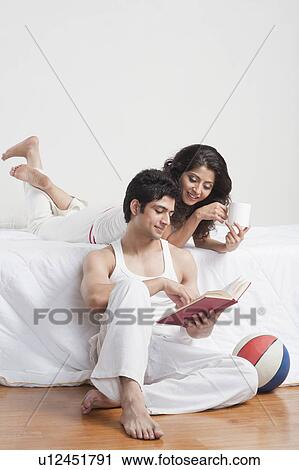 Stock Image - Couple reading a book in a bedroom. Fotosearch