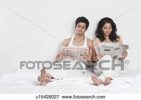 Stock Photo - Couple reading newspaper on the bed. Fotosearch