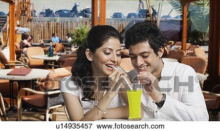 Stock Photo - Couple sharing a glass of juice in a restaurant. Fotosearch