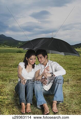 Couple sheltering under an umbrella in a field View Large Photo Image Picture - Couple sheltering under an umbrella in a field. Fotosearch