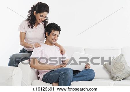 Stock Image - Couple sitting in a couch and using a laptop. Fotosearch