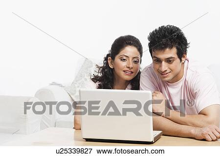 Stock Photo - Couple sitting in a couch and using a laptop. Fotosearch