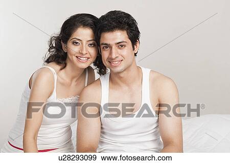 Stock Photo - Couple sitting on the bed and smiling. Fotosearch