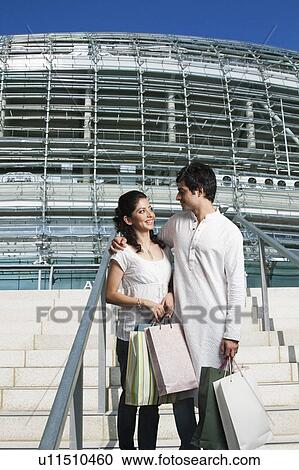 Stock Image - Couple standing on the staircase of a shopping mall. Fotosearch