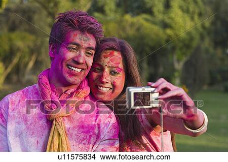Picture - Couple taking a picture of themselves on Holi. Fotosearch