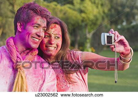 Stock Image - Couple taking a picture of themselves on Holi. Fotosearch