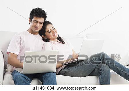 Picture - Couple working on laptops on a couch. Fotosearch