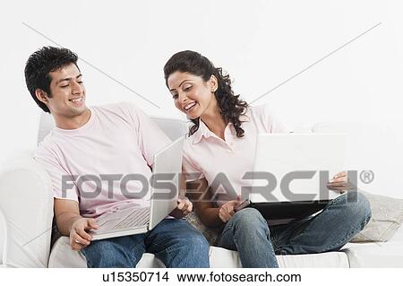 Picture - Couple working on laptops on a couch. Fotosearch