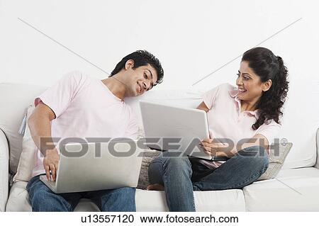 Stock Image - Couple working on laptops on a couch. Fotosearch