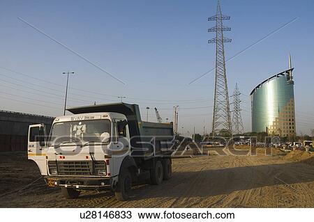 Stock Image - Dump truck on a dirt road with an office building in the background, Gurgaon, Haryana, India. Fotosearch