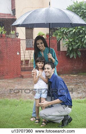 Stock Image - Family enjoying in rain in a park. Fotosearch