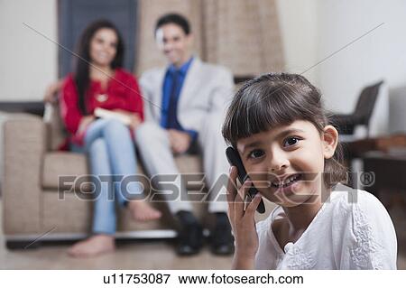 Stock Photo - Girl talking on a mobile phone with her parents sitting in the background. Fotosearch