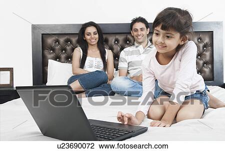 Girl using a laptop with her parents behind her View Large Photo Image Stock Image - Girl using a laptop with her parents behind her. Fotosearch