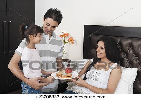 Stock Photo - Girl with her father giving breakfast to her mother. Fotosearch