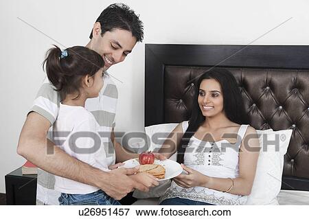 Stock Photo - Girl with her father giving breakfast to her mother. Fotosearch