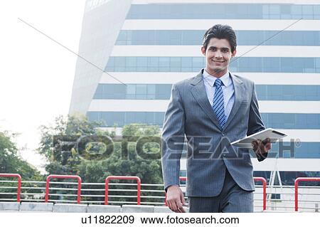 Stock Photo - Happy businessman walking with a digital tablet, Gurgaon, Haryana, India. Fotosearch