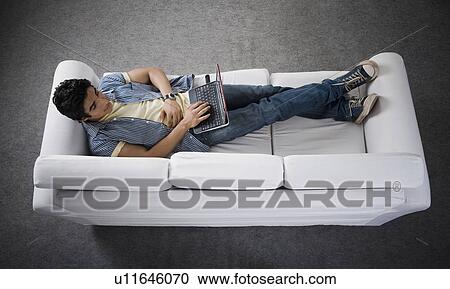 High angle view of a man lying on a couch working on a laptop View Large Photo Image Stock Image - High angle view of a man lying on a couch working on a laptop. Fotosearch
